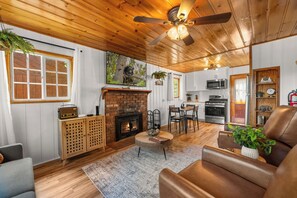 A cozy living room with a fireplace, wooden ceiling, and a dining area with a table and chairs. - Blue Skies- Modern Cabin (Big Bear Lake)