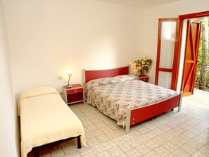 A bedroom with a bed, a bedside table with a lamp, a nightstand, and a window with curtains. - Charming Family Villa in Lignano (Lignano Sabbiadoro)