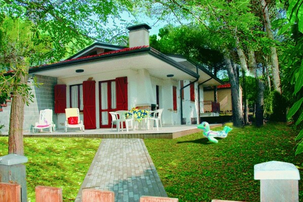 A house with a covered porch, a brick wall, and a lawn. - Charming Family Villa in Lignano (Lignano Sabbiadoro)