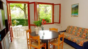 A dining area with a round table, chairs, a vase with flowers, and a sofa. - Charming Family Villa in Lignano (Lignano Sabbiadoro)