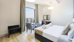 Ein Hotelzimmer mit einem großen Bett, einem Schreibtisch, zwei Stühlen, einer Bank und einem großen Fenster mit Vorhängen.