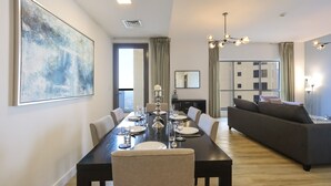 Een moderne eetruimte met een lange tafel voor zes personen, een donkere bank en een groot abstract schilderij aan de muur.