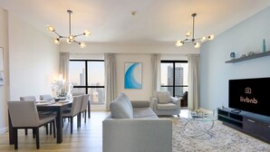 Una sala de estar moderna con comedor, ventanas amplias, televisor de pantalla plana y vista a la ciudad.