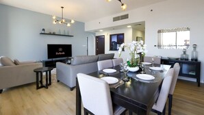 A modern living room with a sofa, dining table set for six, and a TV displaying 'livbnb'. - Livbnb High Floor 2B  Marina View | Walk to Beach (Dubai)