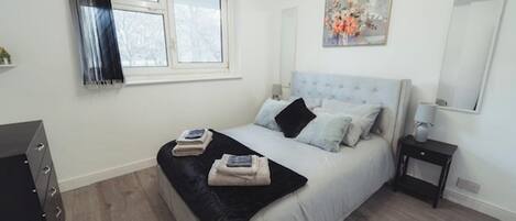 A bedroom with a bed, a nightstand, a dresser, a window, and a painting on the wall.