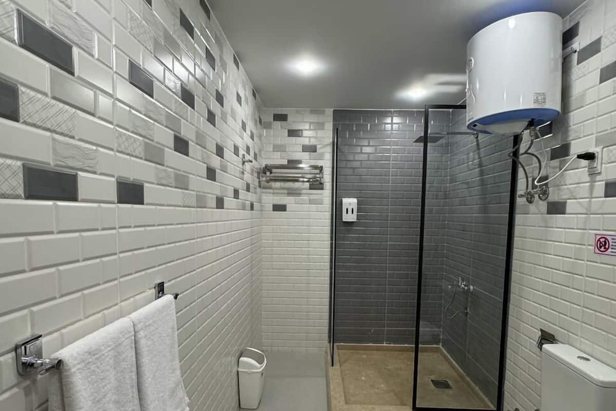 A modern bathroom with white and gray tiles, a glass-enclosed shower, a toilet, and a towel rack.