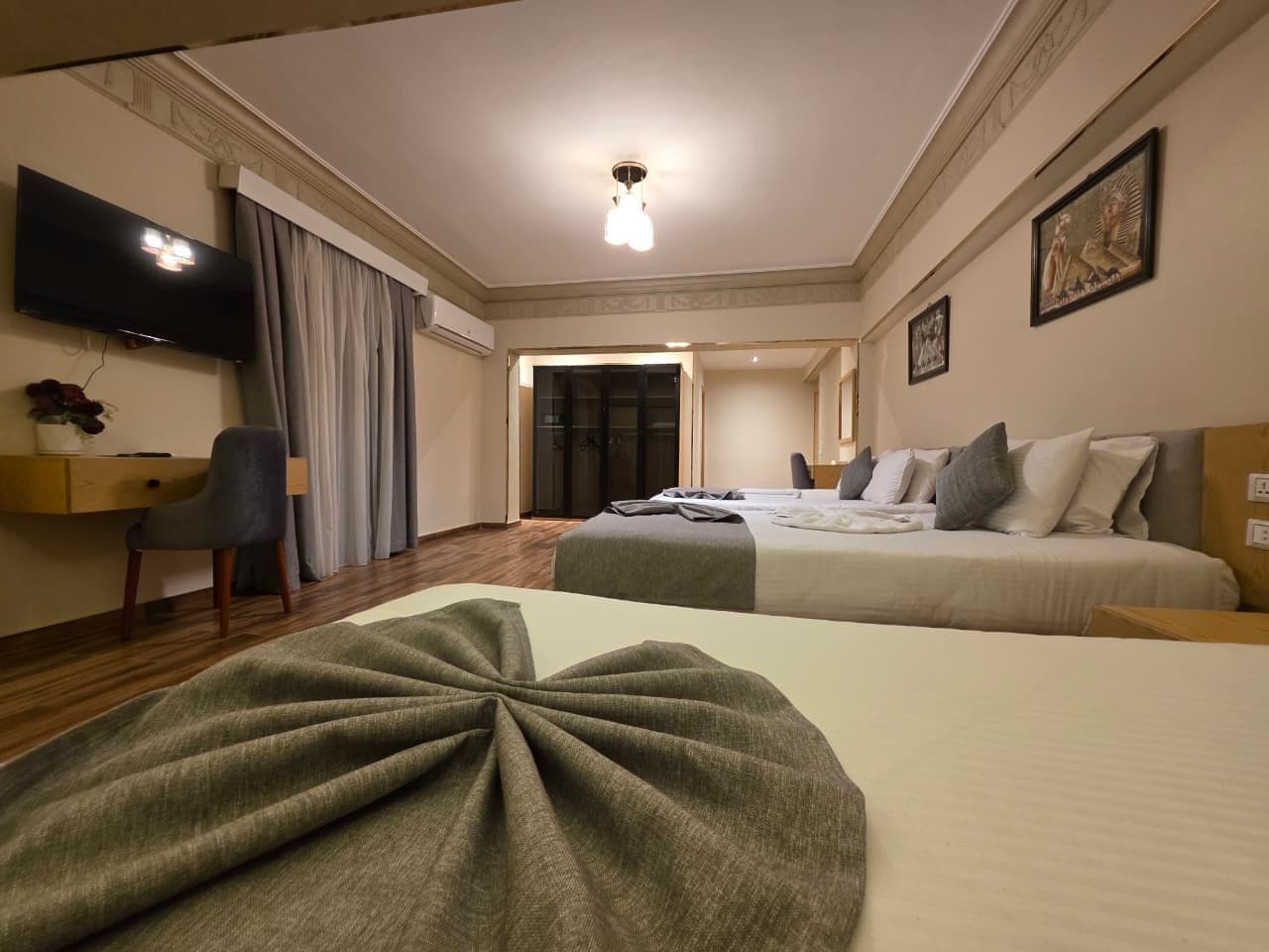 Habitación de hotel con dos camas, un escritorio, un televisor y una puerta que da a otra habitación.
