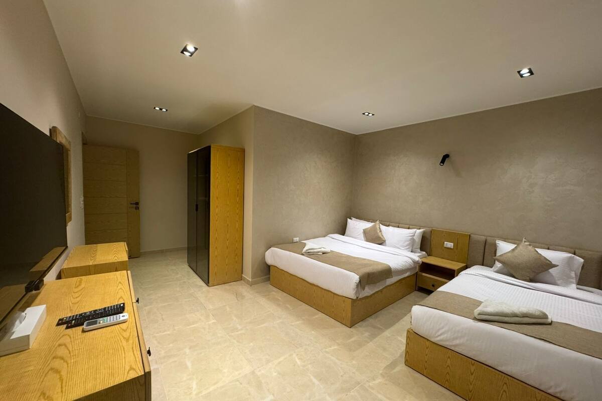 A modern hotel room with two beds, a wooden desk, and a TV.
