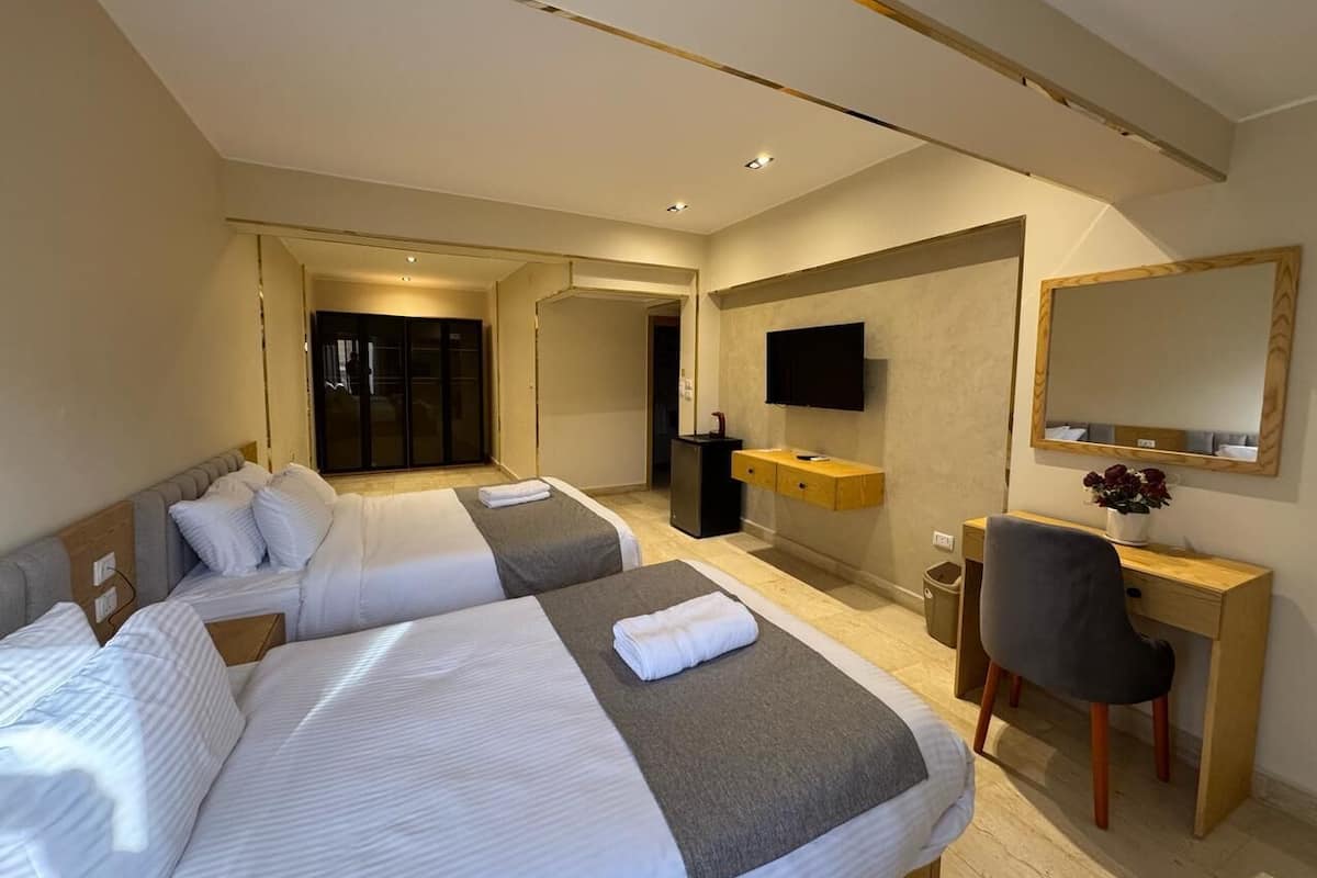 A hotel room with two beds, a desk, a chair, a TV, and a mirror.