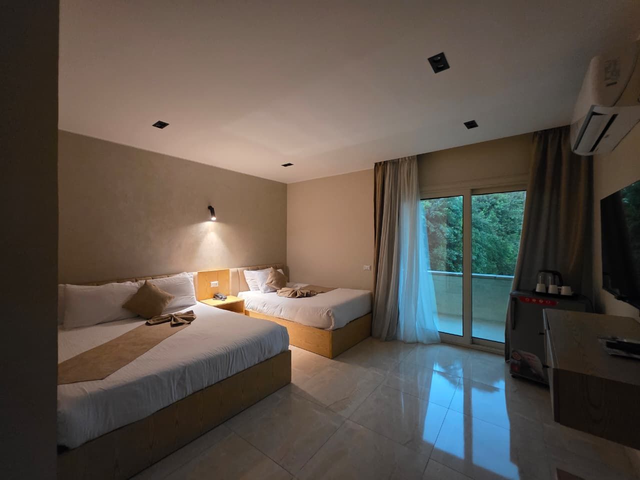 A hotel room with two beds, a TV, and a balcony with curtains.