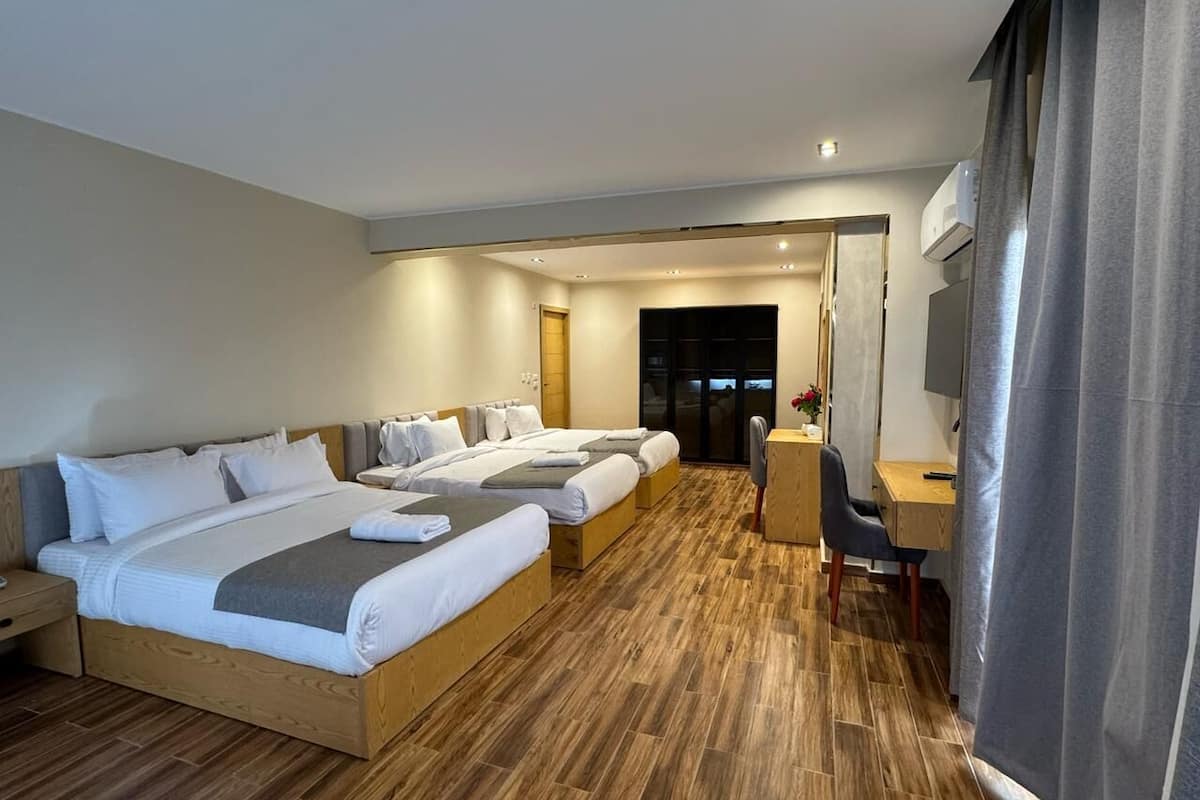 A hotel room with three beds, a desk, and a chair.