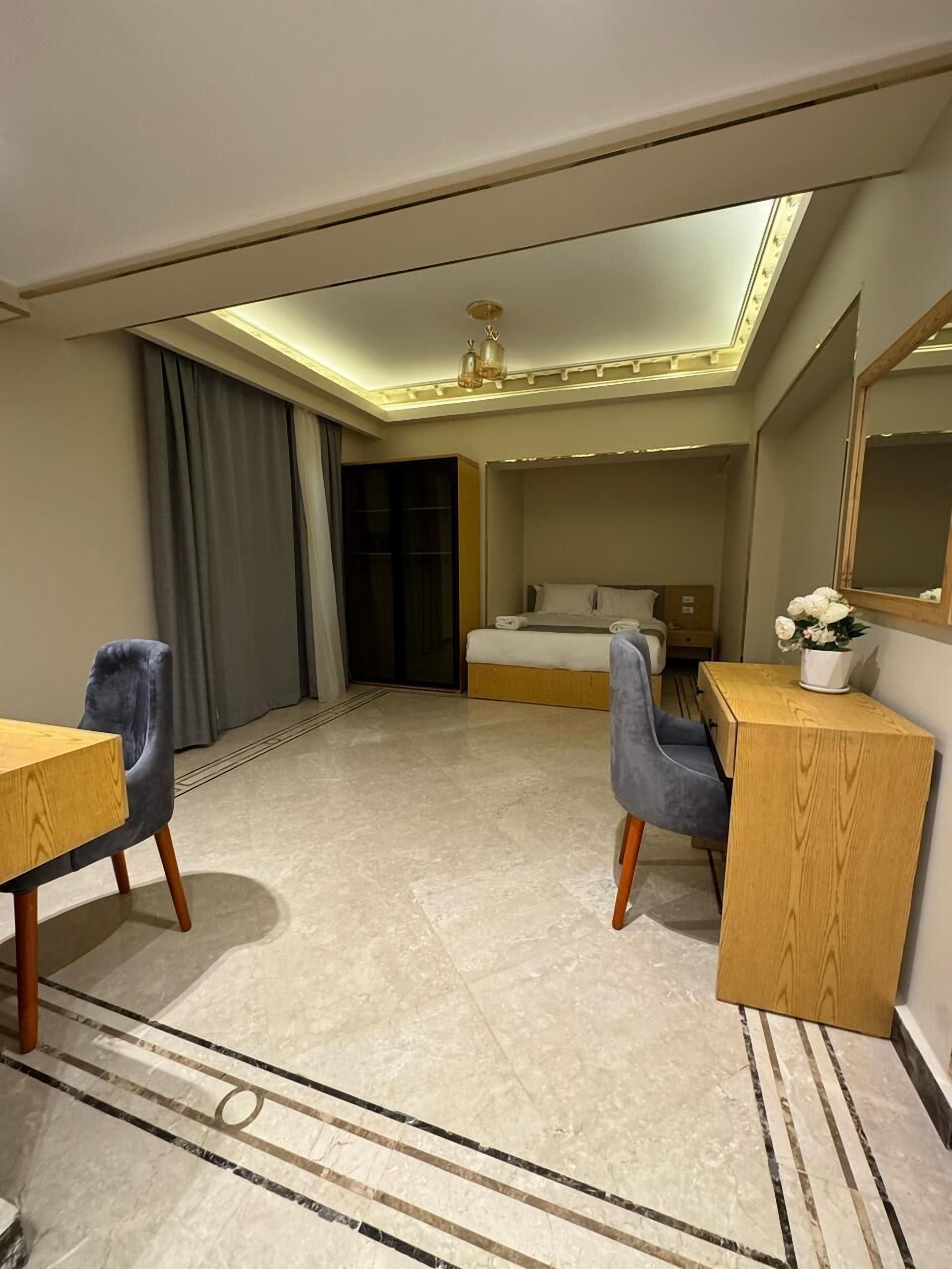 A hotel room with a bed, a desk, a chair, a mirror, and a small table with a flower vase.