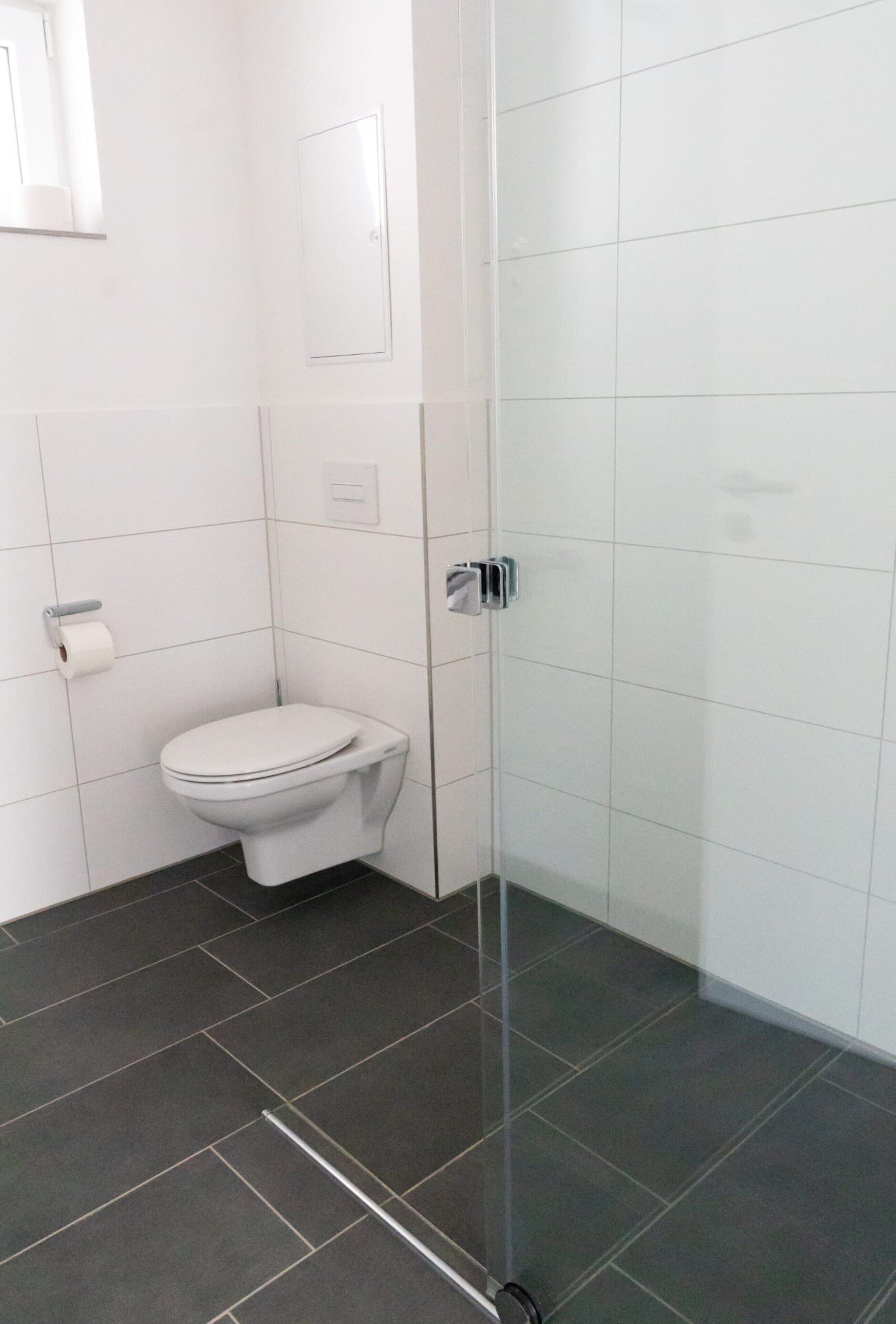 Une salle de bain moderne avec des toilettes, une douche à parois de verre et un carrelage foncé.