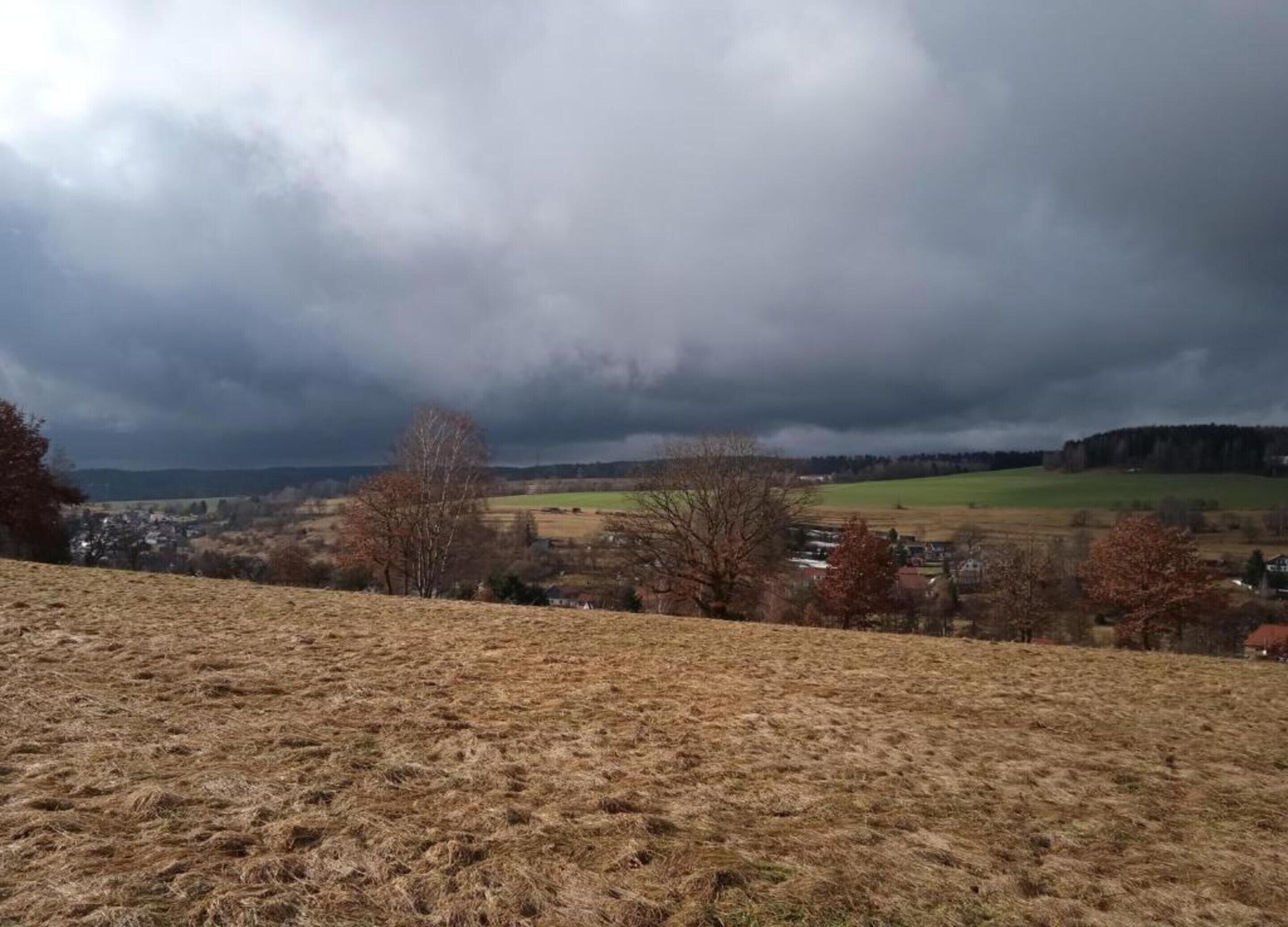 A rural landscape with a view of a village and fields under a cloudy sky.
