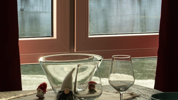 A dining table with a glass bowl, wine glass, and plates, set against a window with a view of a snowy landscape. - Modern Holiday Apartment With Lake View (Harzgerode)