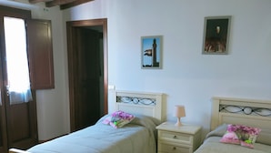 A bedroom with two single beds, a nightstand with a lamp, a wooden door, and a window with curtains.