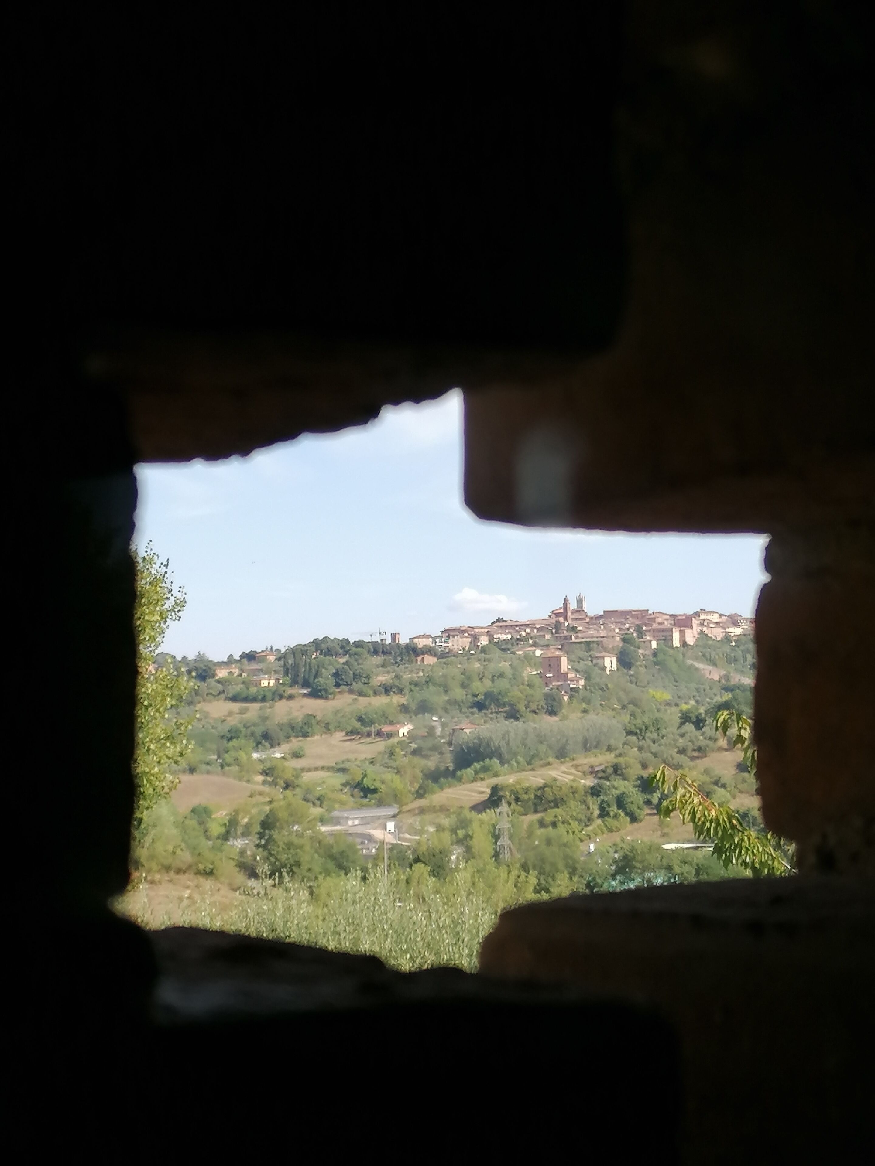 A view through a window of a town with buildings on a hill, greenery, and a clear sky.