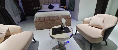 A modern bedroom with a large bed, a brown sofa, a round table with a vase, and two armchairs.