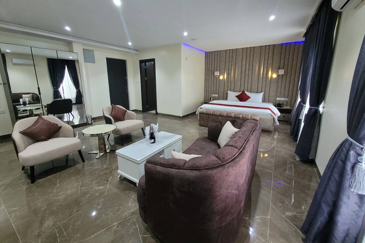 A modern hotel room with a bed, two sofas, a coffee table, and a seating area with a chair.