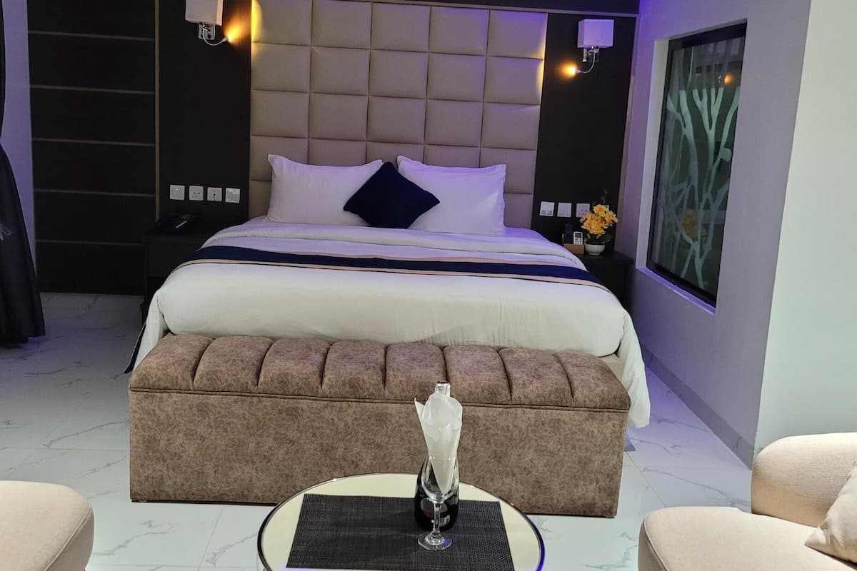 A modern hotel room with a large bed, a round side table, and two armchairs.