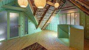 Un ático espacioso con techos altos, vigas de madera, paredes verdes y dos lámparas colgantes.