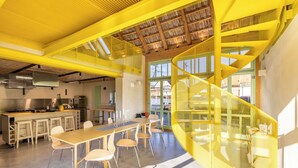 Una cocina amplia con electrodomésticos modernos, un comedor con una mesa larga y sillas, y una escalera de color amarillo brillante.