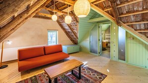 Habitación en el ático con techo de madera, un sofá rojo, una mesa de madera y lámparas colgantes.