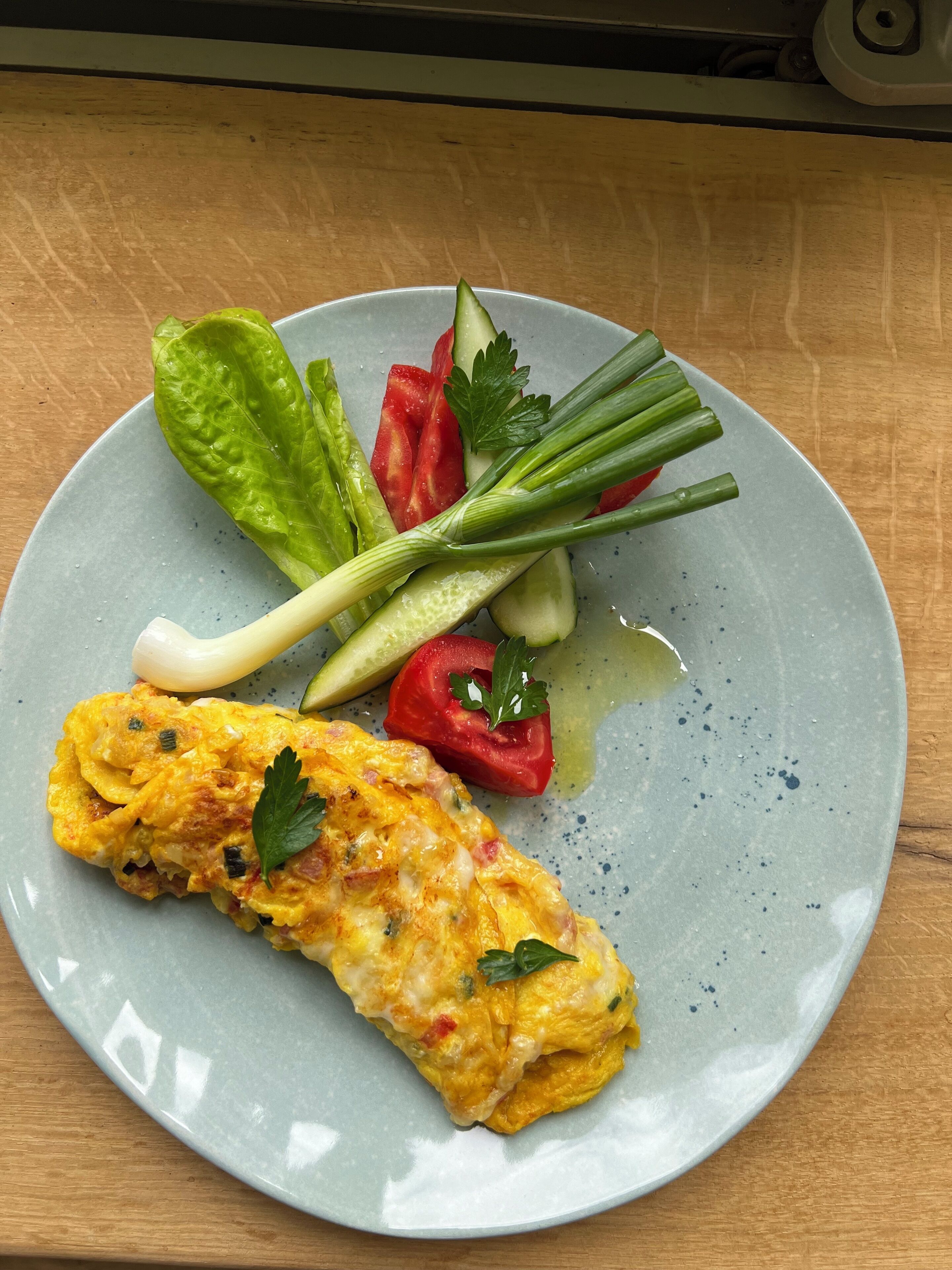 A plate with an omelette, lettuce, cucumber, tomato, and green onions.