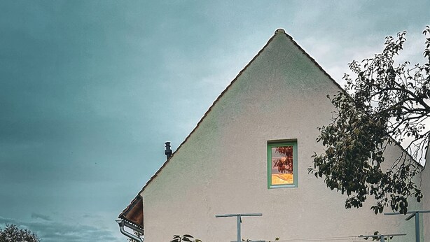 Una casa con un brasero al frente, una puerta verde y un ventanal pequeño.
