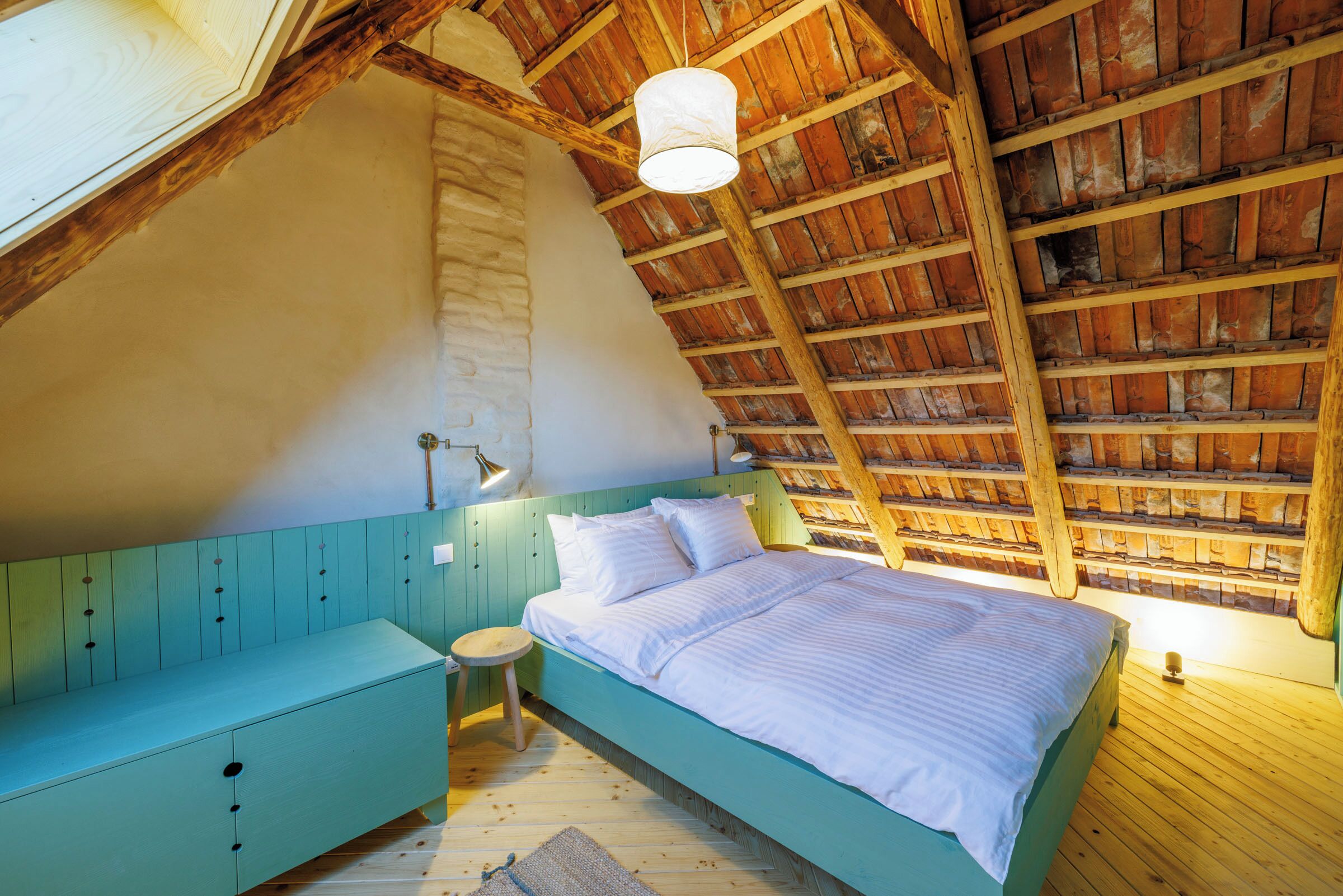 A bedroom with a sloped ceiling, a bed, a bench, and a small stool.