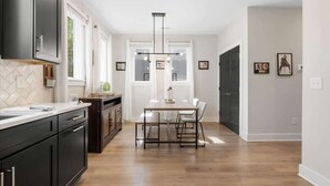 Una cocina moderna con armarios oscuros, una mesa de comedor de madera e iluminación colgante.