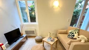 A modern living room with a flat-screen TV, a beige sofa with a decorative pillow, a small wooden side table, and a woven pouf. - Studio 3 persons 50m from Grande Plage Surf (Biarritz)