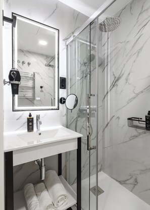 A modern bathroom with a glass-enclosed shower, a white marble sink, and a large mirror. - Limehome Madrid Calle de Matilde Diez (Madrid)