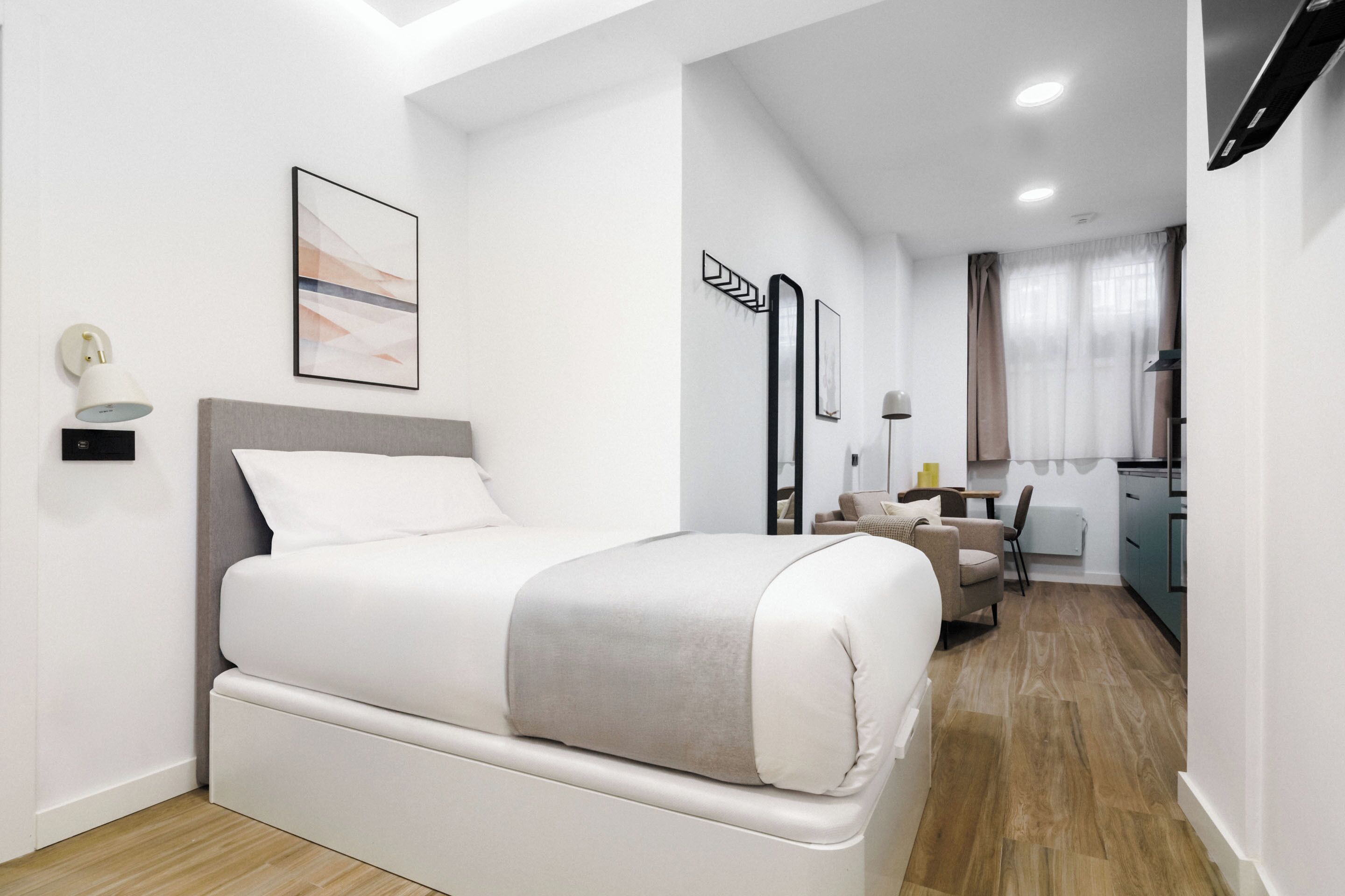 A modern hotel room with a bed, a desk, and a kitchenette.