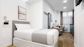 A modern hotel room with a bed, a desk, and a kitchenette.