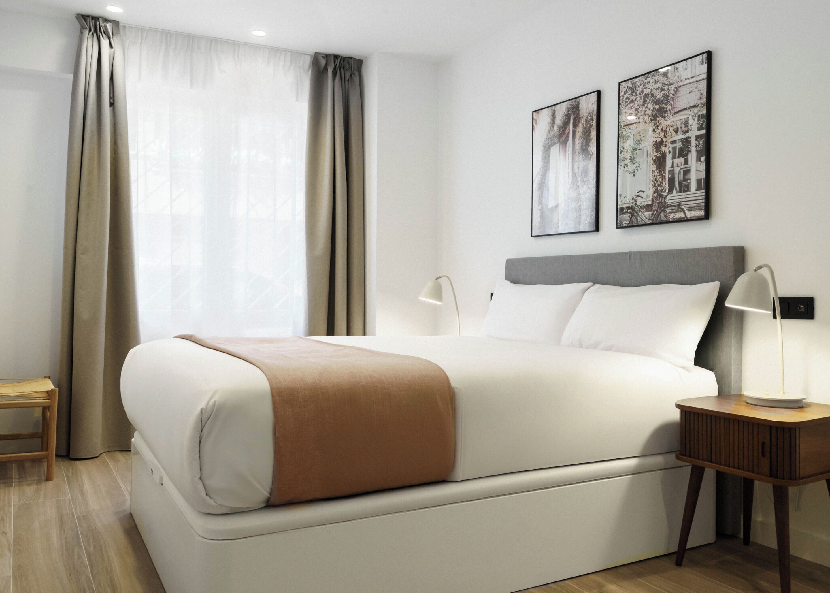 A modern hotel room with a large bed, a bedside table with a lamp, and two framed pictures on the wall.