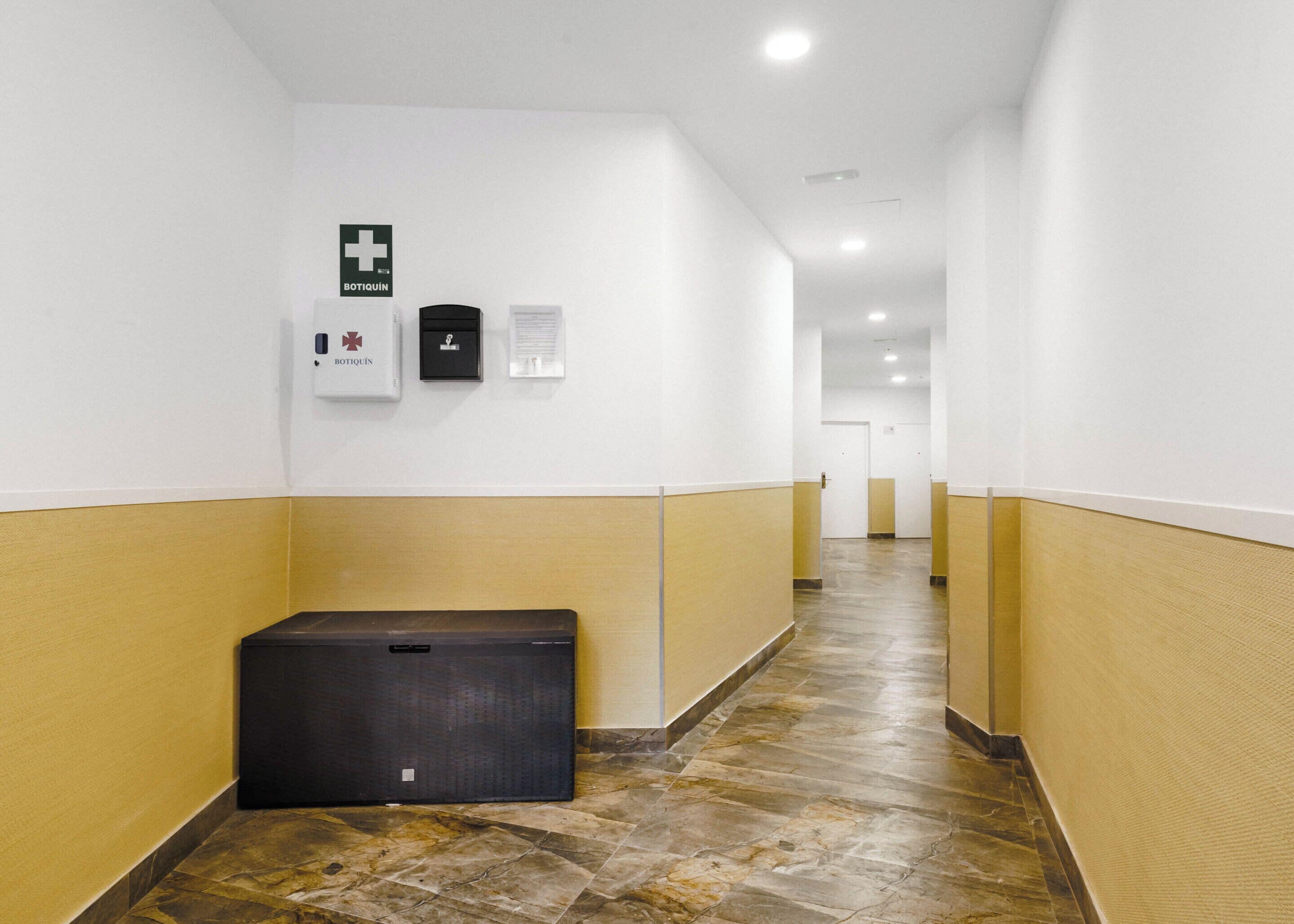 Un pasillo con un letrero de emergencia médica, un botiquín de primeros auxilios y un cubo de basura.