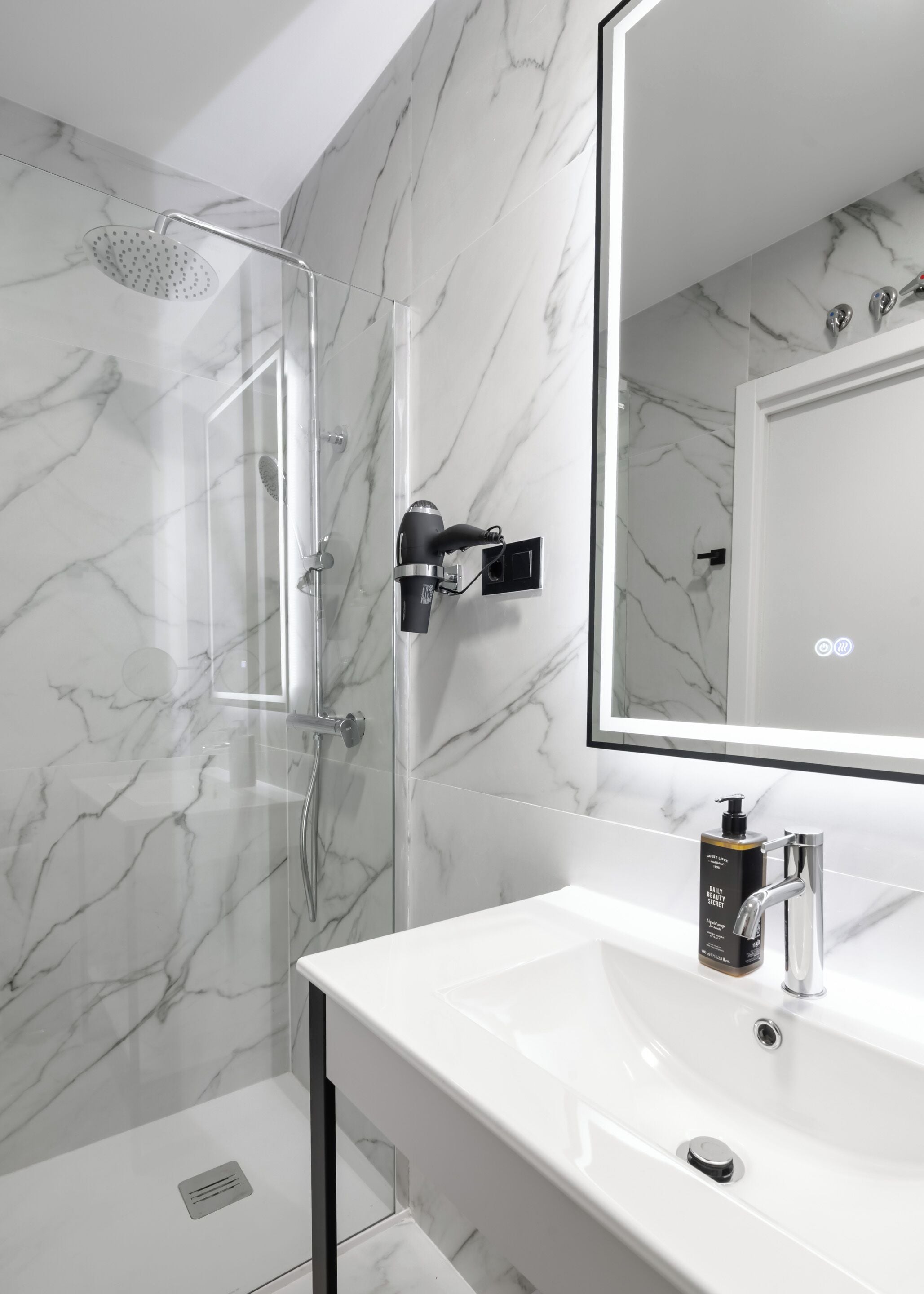 A modern bathroom with a glass-enclosed shower, a white sink with a soap dispenser, and a large mirror.