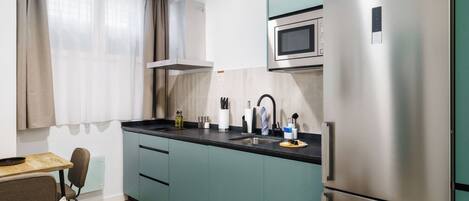 Una cocina moderna con armarios color turquesa, un refrigerador de acero inoxidable y un microondas.