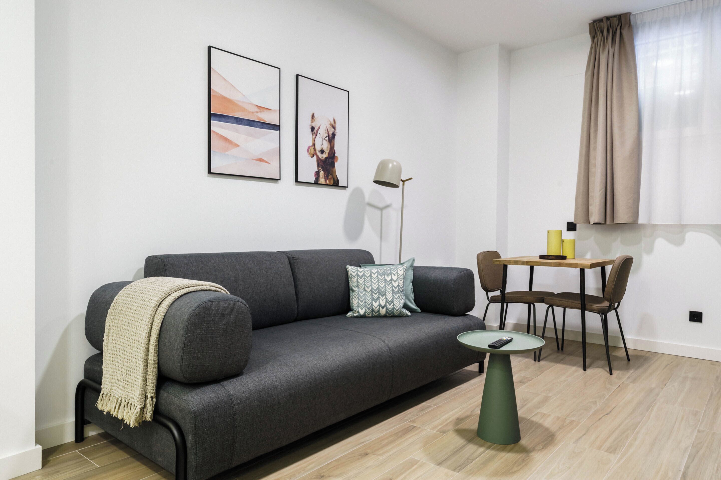Ein modernes Wohnzimmer mit einem grauen Sofa, einem kleinen runden Tisch und einem Essbereich mit Stühlen.