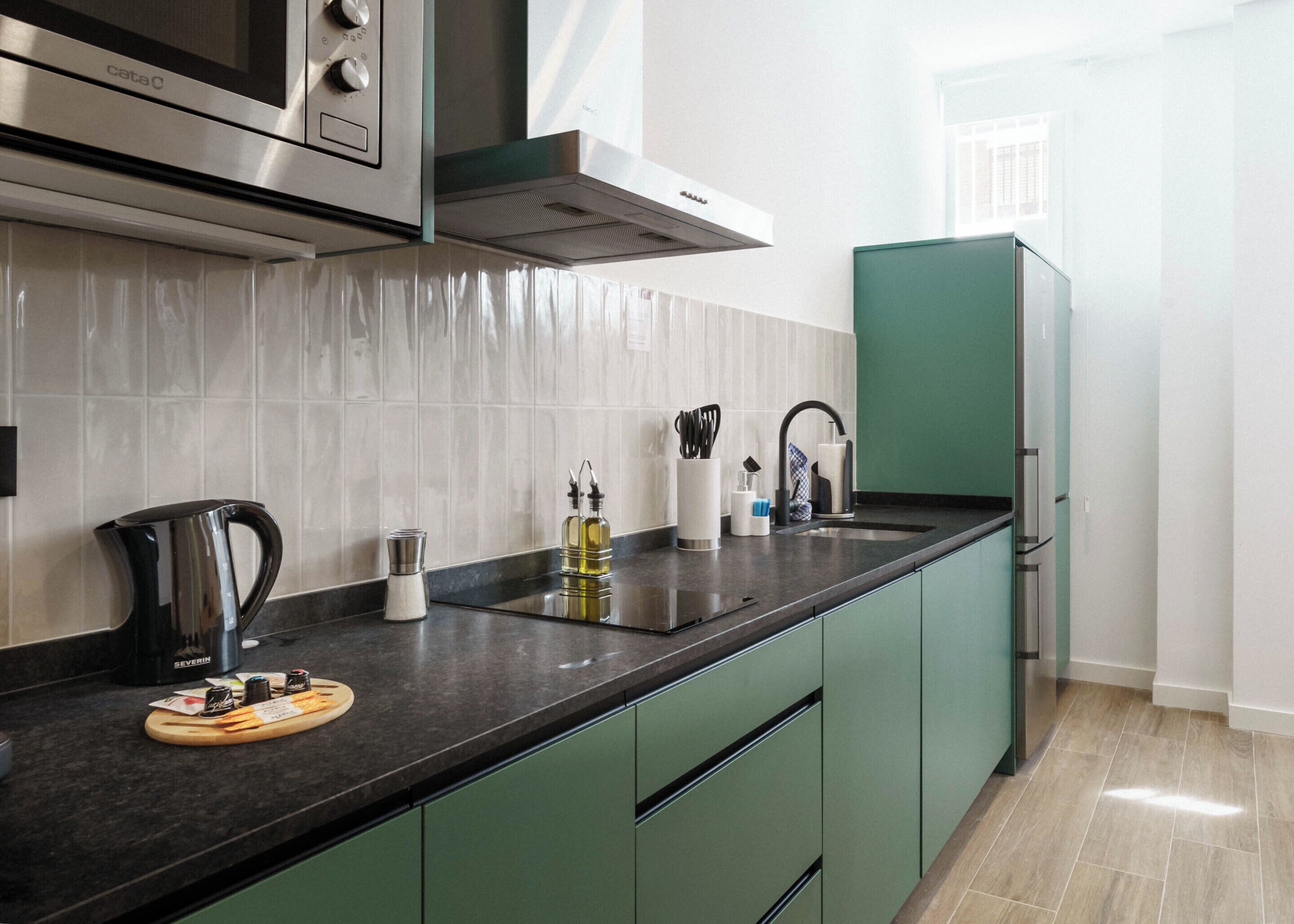 A modern kitchen with a stainless steel microwave, a built-in oven, a range hood, and a green cabinet.