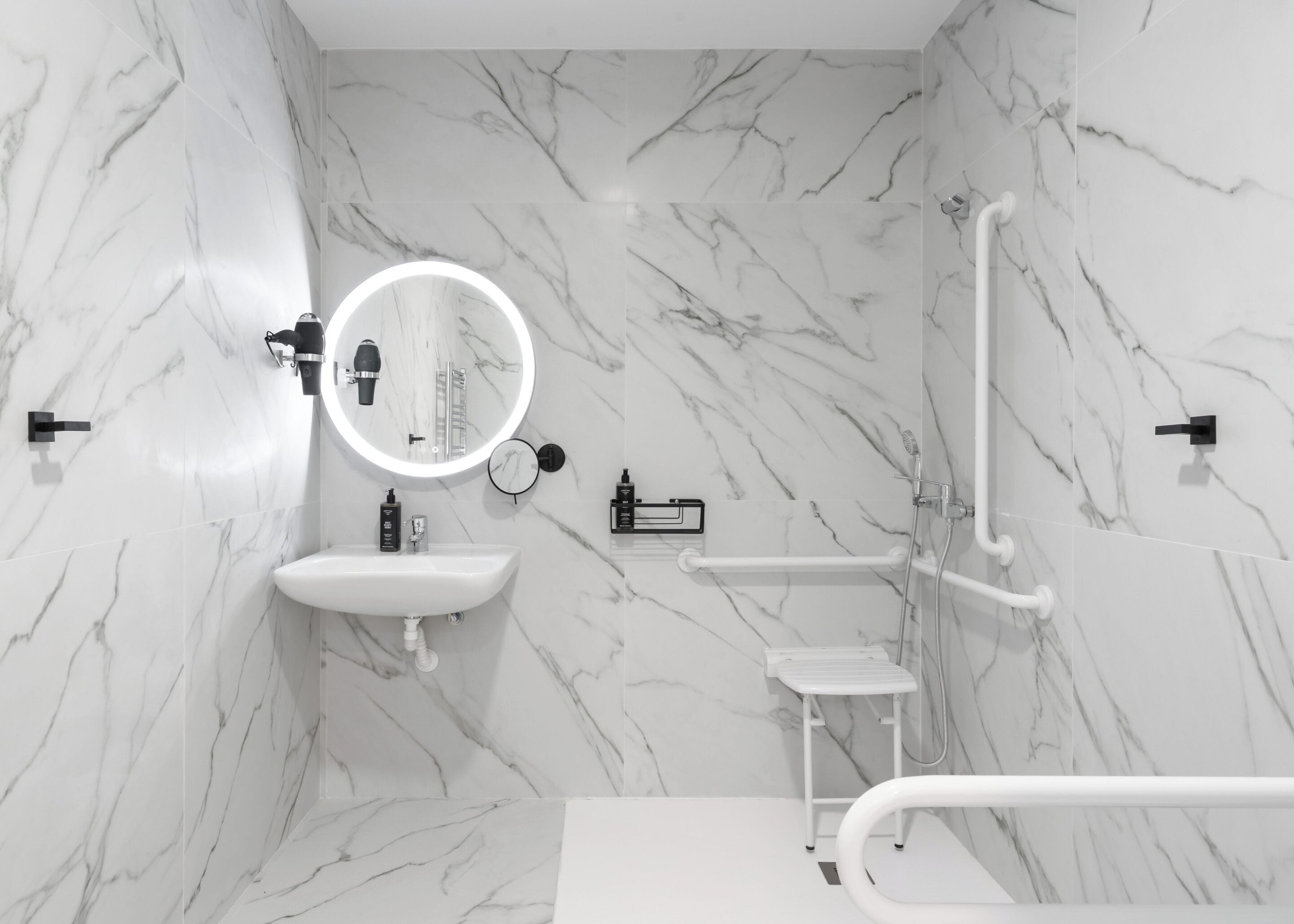 Un baño moderno con paredes de mármol, un espejo redondo, un lavabo y una zona de ducha.