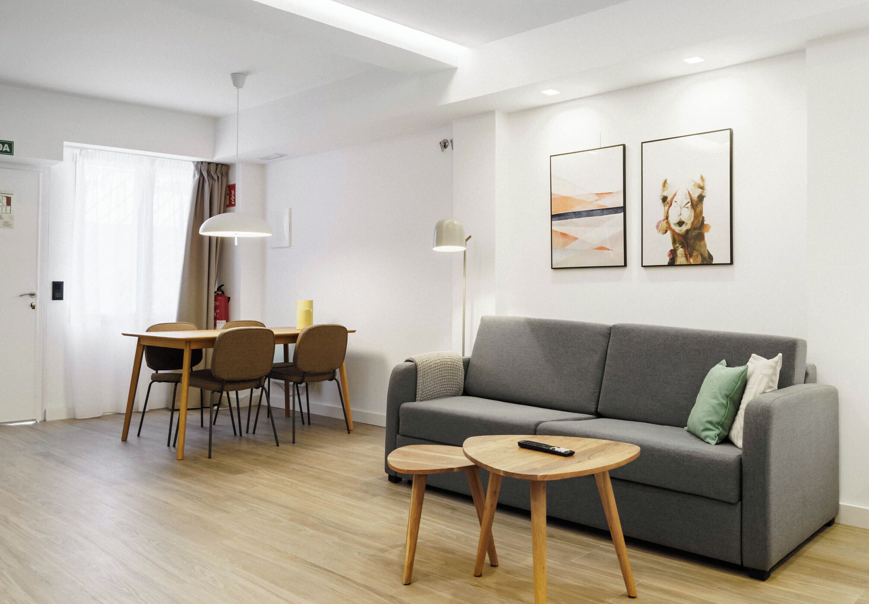 Una sala moderna con un sofá gris, una mesa de comedor de madera y dos mesitas auxiliares.