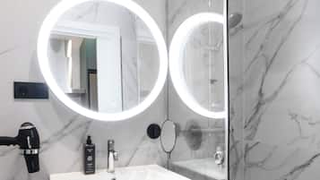 A modern bathroom with a glass-enclosed shower, a white sink, and two round mirrors with built-in lighting.