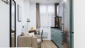 A compact hotel room with a bed, a sofa, a dining area with a table and chairs, a kitchenette with a refrigerator, and a window with curtains. - Limehome Madrid Calle de Matilde Diez (Madrid)