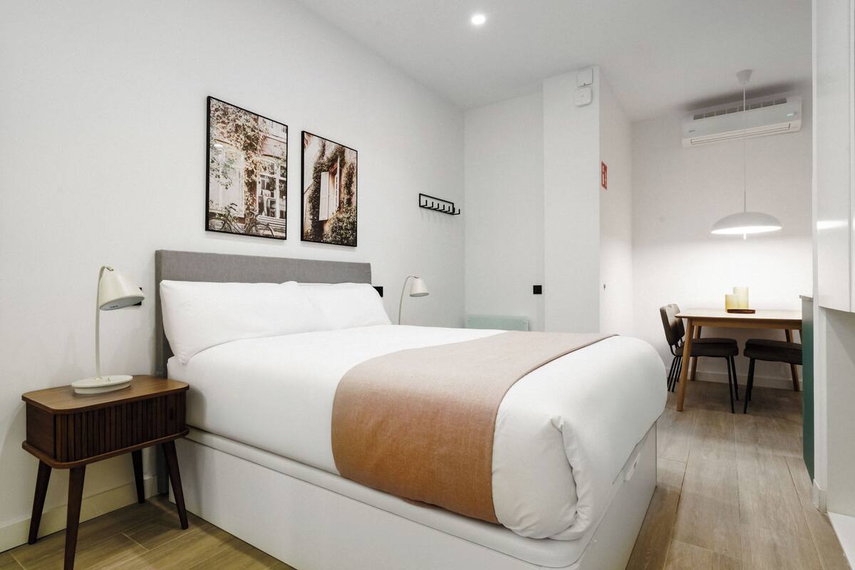A neatly arranged hotel room with a bed, bedside tables, a desk, and chairs.