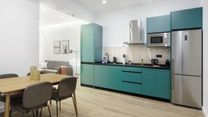 A modern kitchen with teal cabinets, stainless steel appliances, and a wooden dining table with chairs. - Limehome Madrid Calle de Matilde Diez (Madrid)