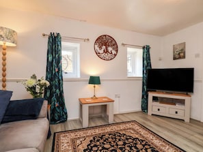 A living room with a sofa, a TV, a small table with a lamp, a decorative wall piece, and curtains.