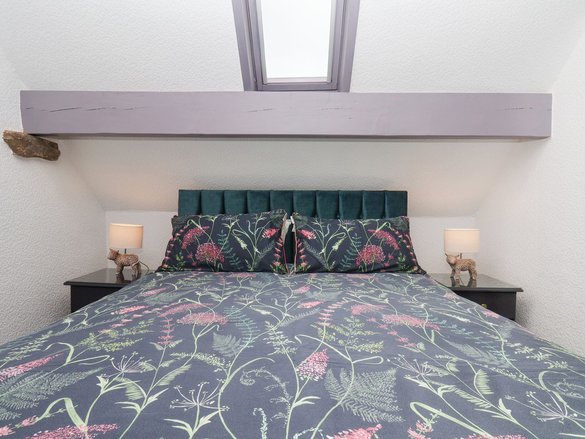 Un dormitorio con cama, dos lámparas de noche, una ventana y cabecera.