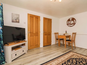 A room with a TV, wooden doors, a dining table with chairs, and a decorative wall piece.